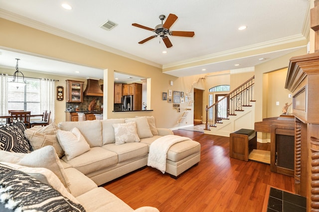 living room featuring crown molding, visible vents, ceiling fan, wood finished floors, and stairs