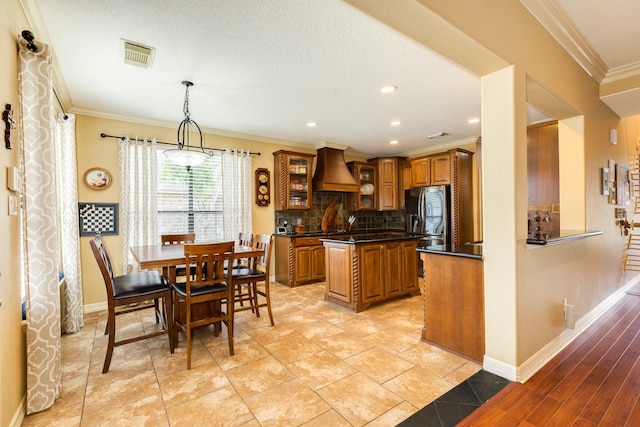 kitchen featuring brown cabinets, custom range hood, crown molding, visible vents, and dark countertops