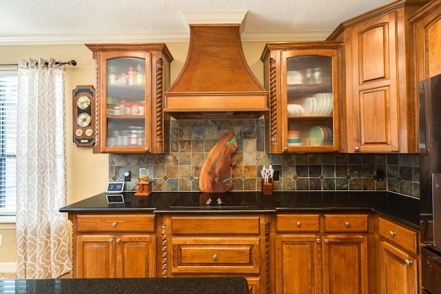 kitchen with premium range hood, a textured ceiling, backsplash, and glass insert cabinets