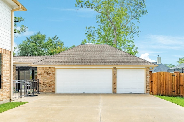 view of front facade with fence, roof with shingles, brick siding, and a garage