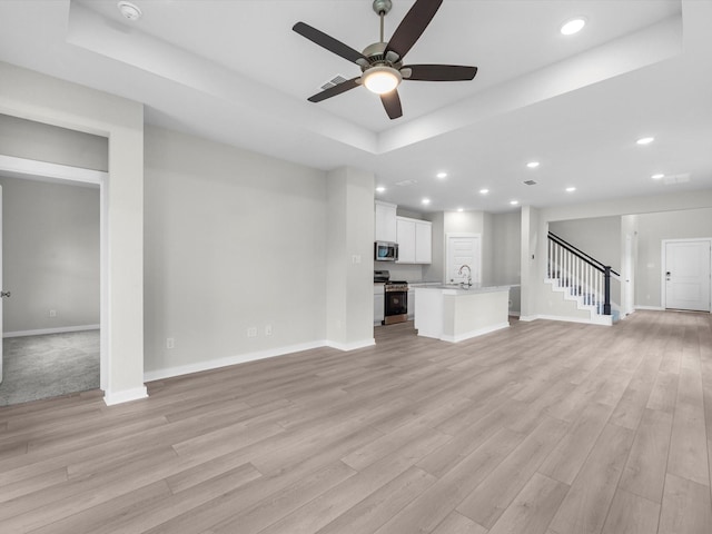 21711 White Bellflower Ln, Cypress, TX 77433 - unfurnished living room with a tray ceiling, ceiling fan, stairway, light wood-style floors, and recessed lighting
