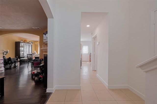hall featuring arched walkways, visible vents, tile patterned floors, and baseboards