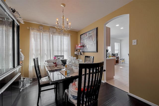 dining room featuring arched walkways, a notable chandelier, wood finished floors, and baseboards