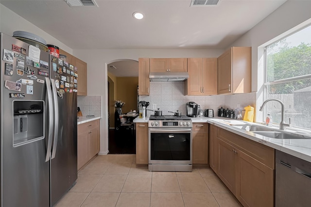 kitchen featuring arched walkways, decorative backsplash, stainless steel appliances, under cabinet range hood, and a sink