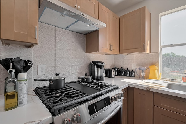 kitchen featuring stainless steel gas range, light stone counters, under cabinet range hood, and tasteful backsplash