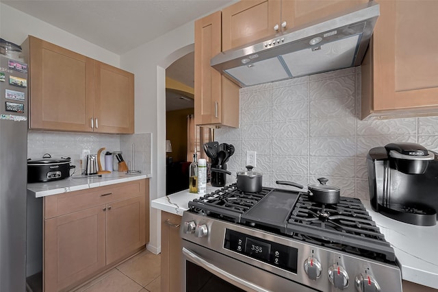 kitchen featuring arched walkways, decorative backsplash, stainless steel appliances, under cabinet range hood, and light countertops
