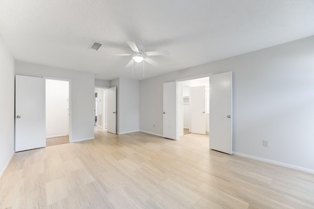unfurnished bedroom featuring visible vents, ceiling fan, baseboards, light wood finished floors, and a walk in closet