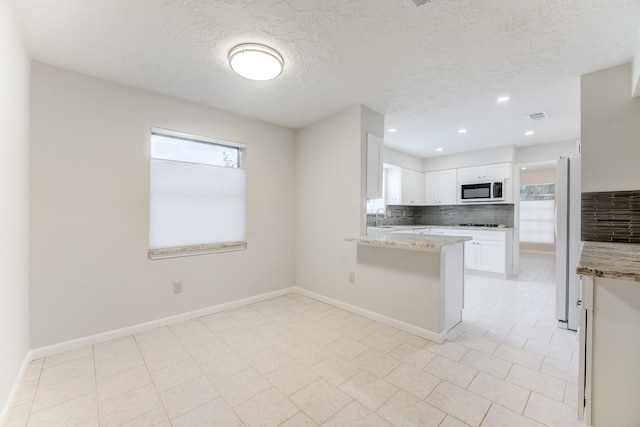 kitchen featuring white cabinetry, plenty of natural light, freestanding refrigerator, and backsplash