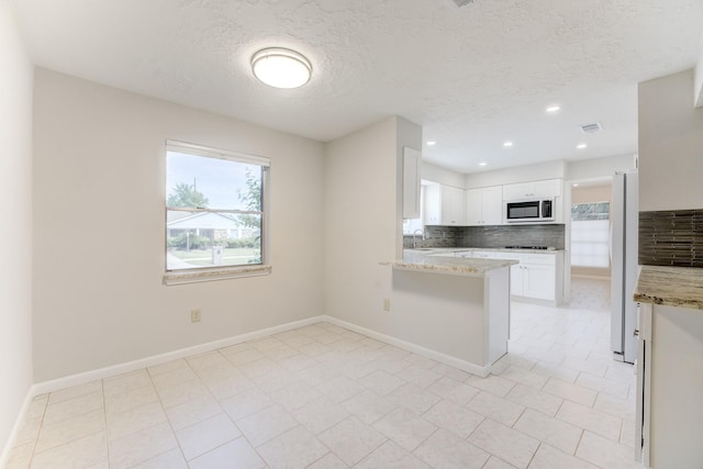 kitchen featuring tasteful backsplash, a peninsula, a textured ceiling, white cabinets, and freestanding refrigerator
