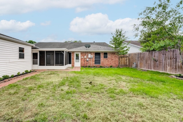 back of property featuring brick siding, fence private yard, a shingled roof, a sunroom, and a lawn