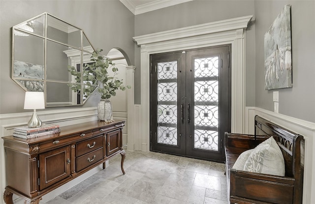 entryway with ornamental molding, wainscoting, a decorative wall, french doors, and arched walkways