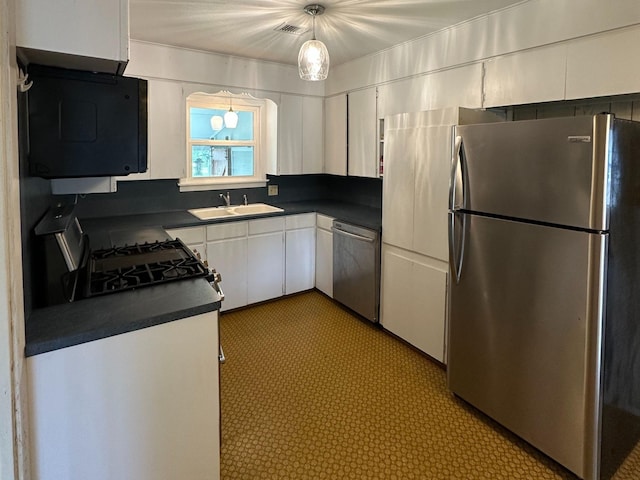kitchen with appliances with stainless steel finishes, dark countertops, a sink, white cabinetry, and visible vents