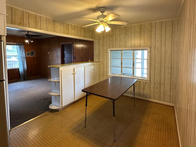 unfurnished dining area featuring wooden walls, a ceiling fan, carpet flooring, and baseboards