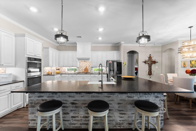 kitchen with a sink, appliances with stainless steel finishes, dark countertops, arched walkways, and dark wood finished floors