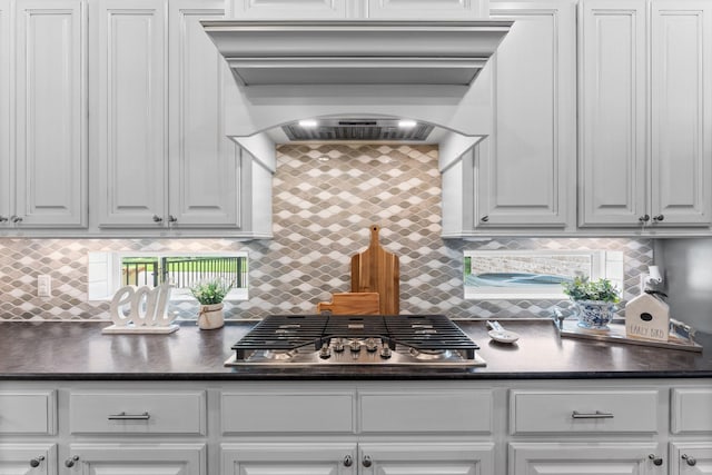 kitchen featuring dark countertops, premium range hood, stainless steel gas cooktop, and white cabinetry