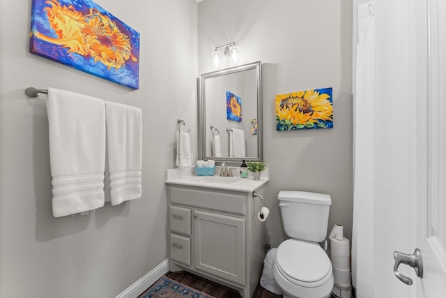 bathroom with baseboards, wood finished floors, toilet, and vanity