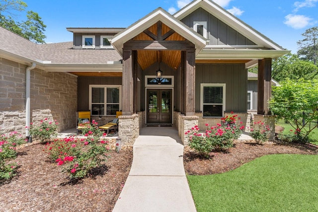 property entrance featuring a shingled roof, covered porch, stone siding, board and batten siding, and french doors