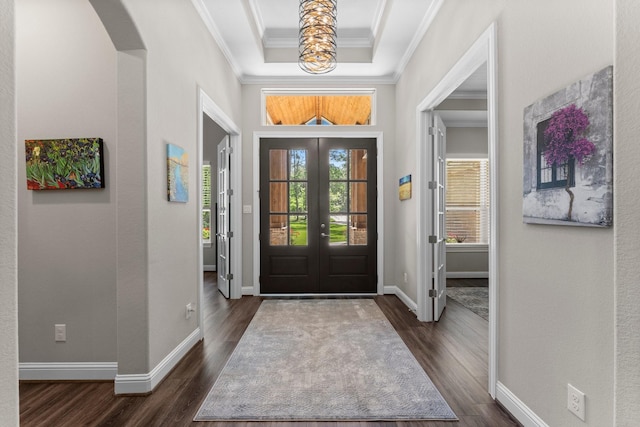 foyer with a raised ceiling, dark wood-style floors, arched walkways, ornamental molding, and french doors