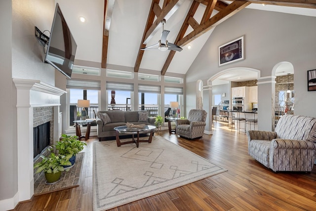 living room with arched walkways, ornate columns, beam ceiling, high vaulted ceiling, and a ceiling fan