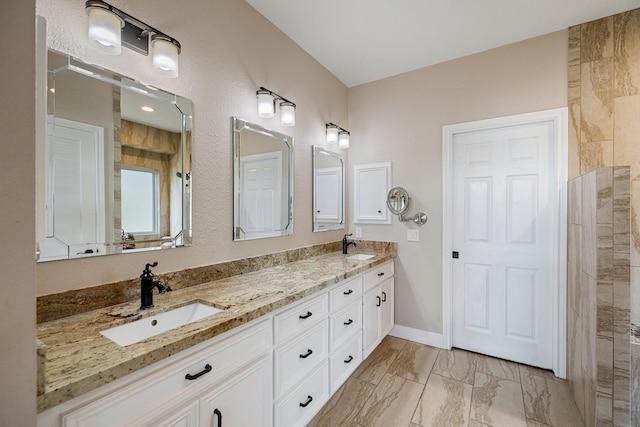full bath with baseboards, marble finish floor, double vanity, and a sink