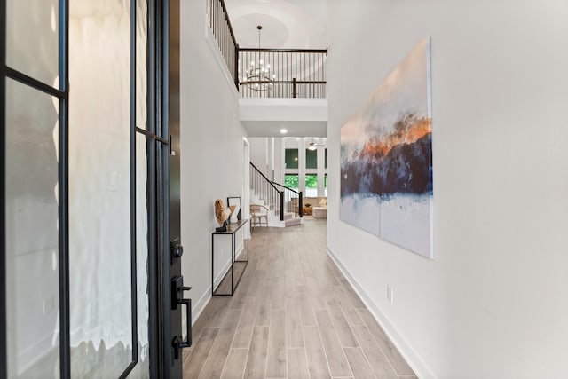 hall featuring a notable chandelier, light wood-style flooring, stairs, baseboards, and a towering ceiling
