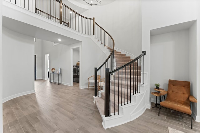 stairway featuring baseboards, a high ceiling, washer / clothes dryer, and wood finished floors