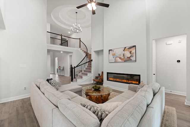 living room featuring a glass covered fireplace, a towering ceiling, wood finished floors, and stairway