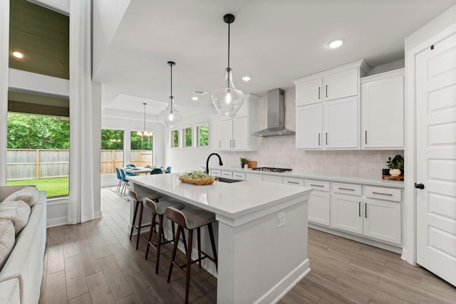 kitchen featuring decorative backsplash, wood finished floors, a center island with sink, wall chimney range hood, and a sink