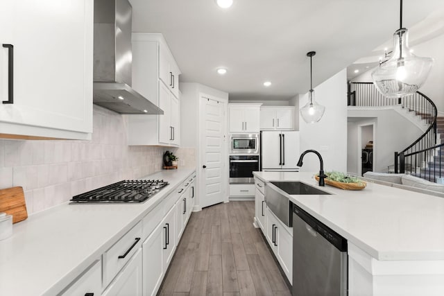kitchen featuring appliances with stainless steel finishes, a sink, light countertops, wall chimney exhaust hood, and light wood-type flooring
