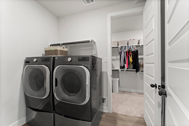 washroom with laundry area, visible vents, wood finished floors, baseboards, and washing machine and clothes dryer