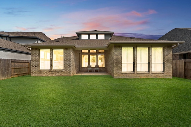 back of property at dusk featuring a patio, a fenced backyard, a lawn, and brick siding