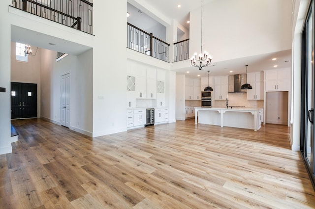 202 Calm Savanna Ct, Conroe, TX 77318 - unfurnished living room featuring a chandelier, a high ceiling, wine cooler, light wood-style flooring, and a sink
