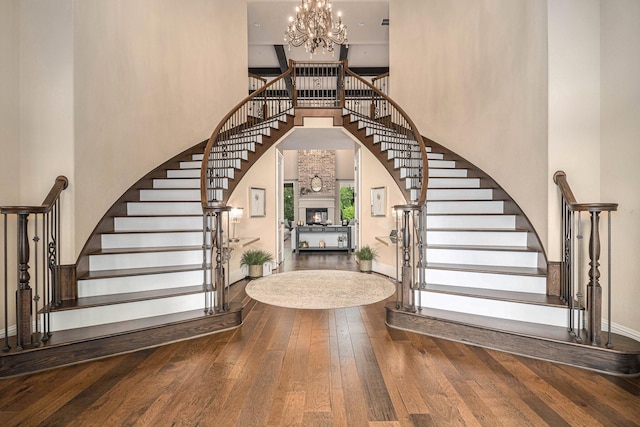 entryway with a high ceiling, stairway, wood-type flooring, a chandelier, and a lit fireplace