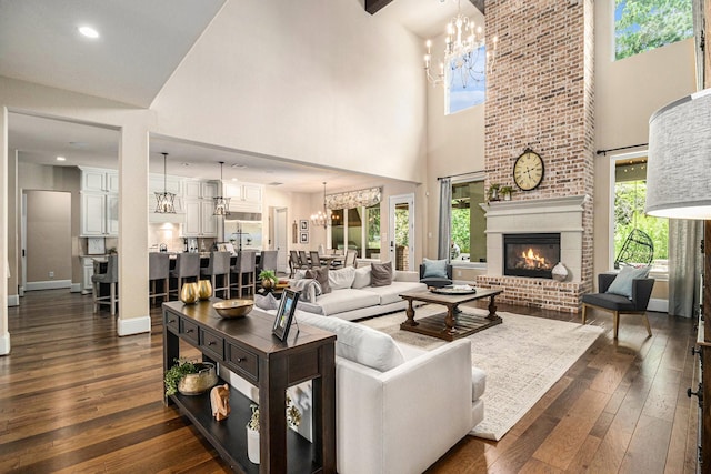 living area with a chandelier, a towering ceiling, dark wood-style flooring, and healthy amount of natural light
