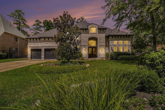 french provincial home featuring brick siding, concrete driveway, an attached garage, a yard, and french doors