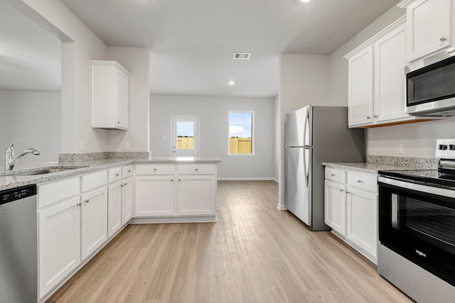kitchen with white cabinetry, a sink, appliances with stainless steel finishes, light wood-style floors, and a peninsula