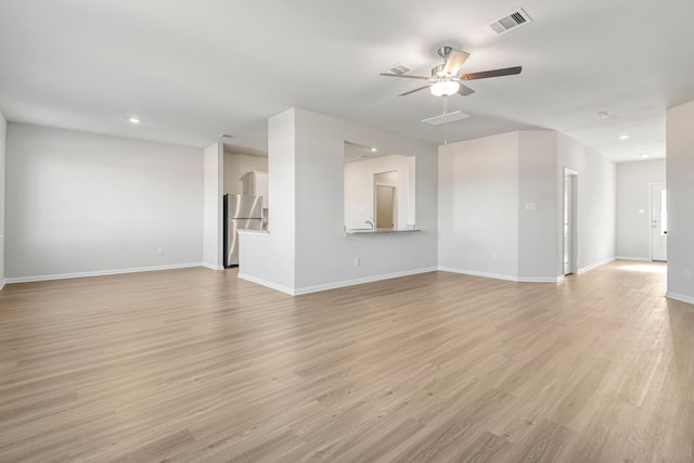 unfurnished living room featuring light wood-type flooring, visible vents, a ceiling fan, and baseboards