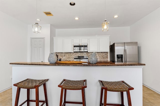 kitchen with visible vents, backsplash, white cabinetry, appliances with stainless steel finishes, and a breakfast bar area