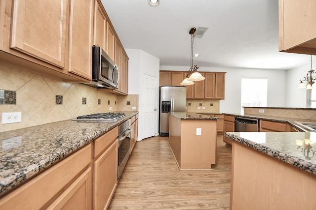 kitchen featuring dark stone countertops, appliances with stainless steel finishes, backsplash, light wood finished floors, and a center island