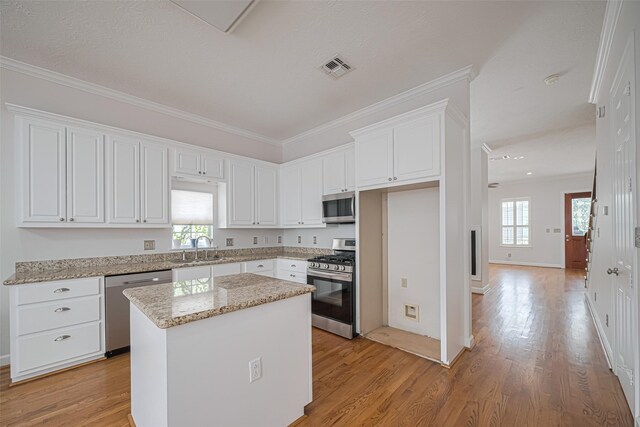 kitchen with white cabinetry, a sink, appliances with stainless steel finishes, a kitchen island, and light wood finished floors