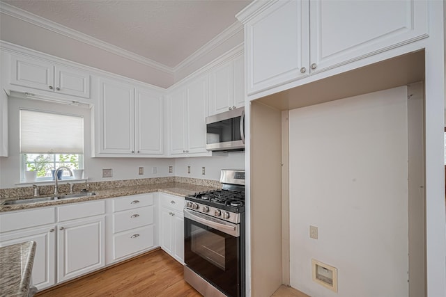 kitchen featuring white cabinetry, light wood-type flooring, stainless steel appliances, and a sink