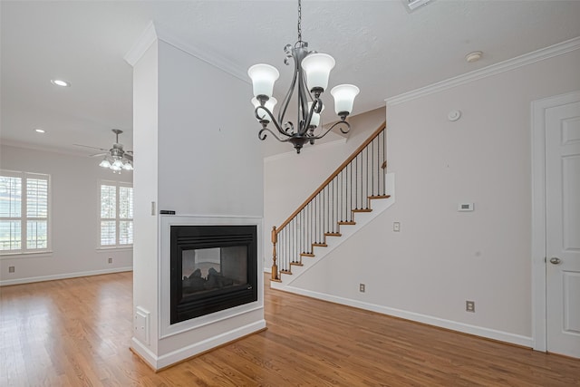 unfurnished living room with light wood finished floors, a multi sided fireplace, crown molding, baseboards, and ceiling fan with notable chandelier