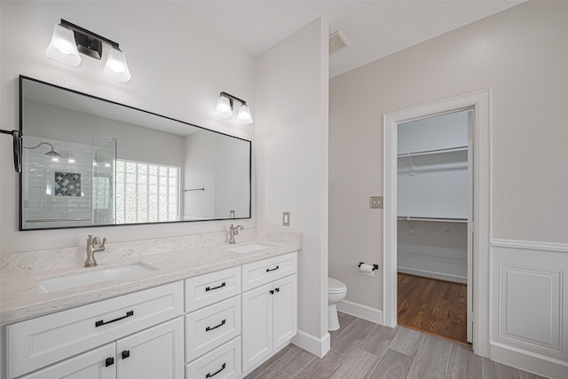 bathroom featuring a tile shower, a sink, wood finished floors, and visible vents