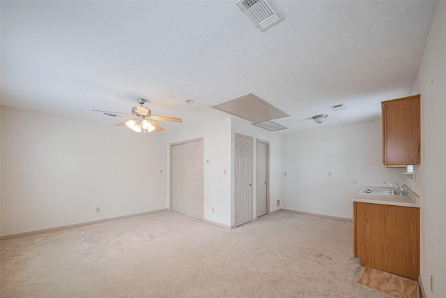 unfurnished living room featuring attic access, visible vents, ceiling fan, and light carpet