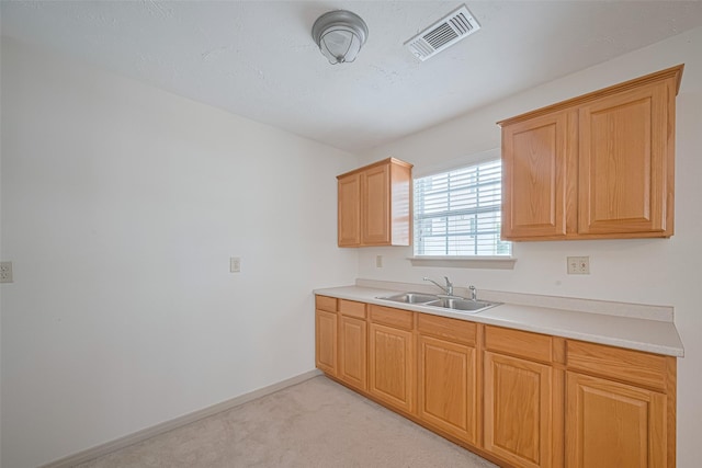 kitchen with a sink, visible vents, baseboards, light carpet, and light countertops