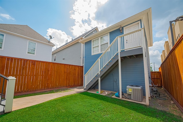 rear view of house featuring a lawn, a fenced backyard, cooling unit, and stairs