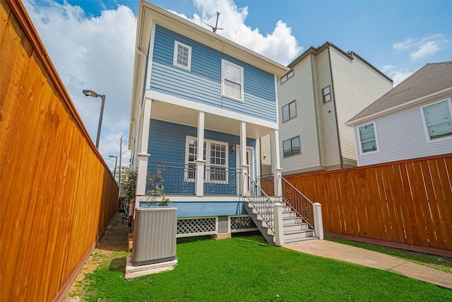 rear view of house featuring covered porch, fence, cooling unit, and a yard
