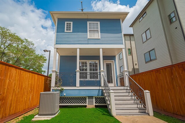 rear view of house with fence, covered porch, central AC, and a yard