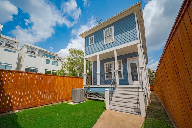 rear view of house featuring covered porch, fence, central AC unit, and a yard