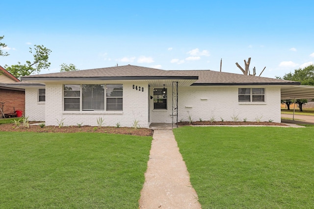 ranch-style house with a shingled roof, an attached carport, a front lawn, and brick siding
